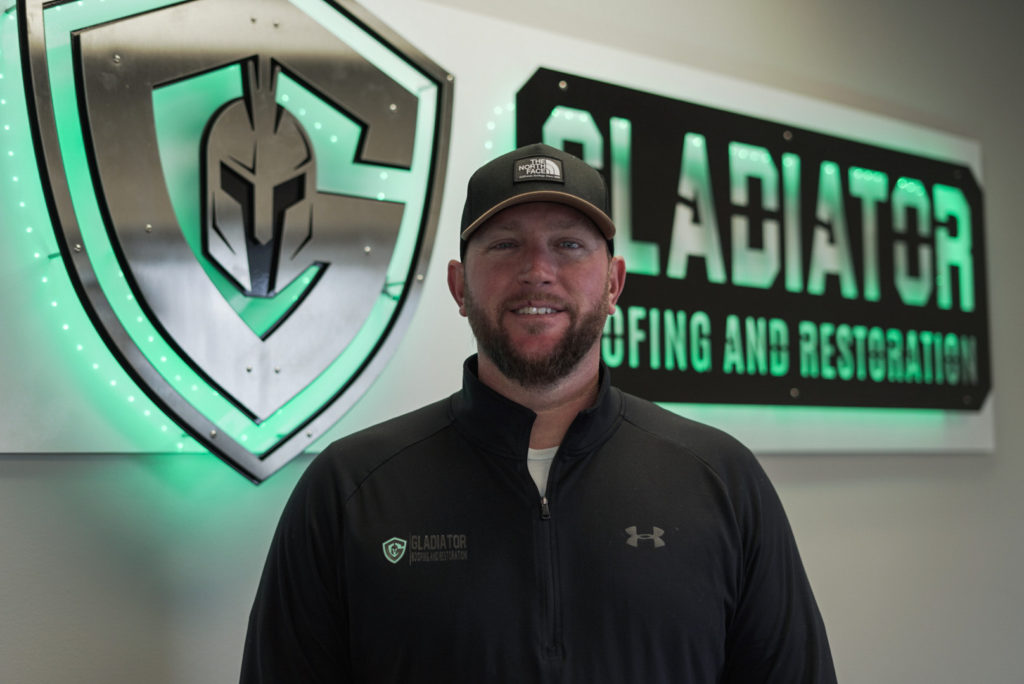 Gladiator Roofing and Restoration Owner, Dustin Rees, Standing in front of company sign